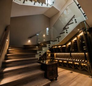 Timber staircase at House 671 with glass balustrades and an illuminated wine display