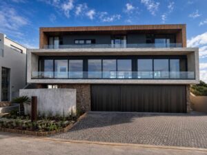 Completed front elevation of House 671 in Stilbaai with stone cladding, timber soffits and glazed balconies