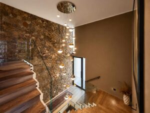 Upper staircase landing at House 671 with a natural-stone feature wall and glass balustrade
