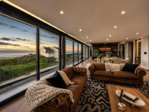 Living room at House 671 with a patterned rug, glazed balcony doors and coastal view
