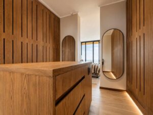 Timber bedroom cabinetry and dressing area at House 671 with an arched doorway and round mirror