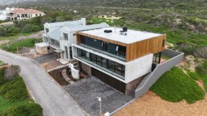 Aerial corner view of House 671 showing the flat roof, front balcony and surrounding coastal vegetation
